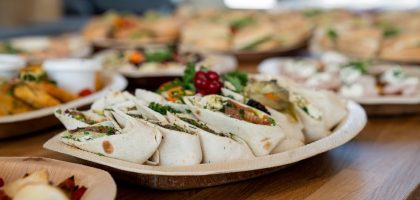 A wooden platter of assorted vegetarian wraps with fresh ingredients, perfect for parties.